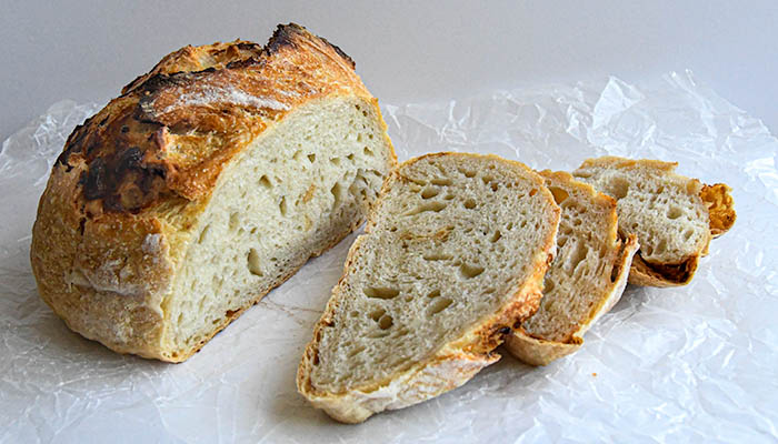 A loaf of no-knead bread studded with garlic, partially sliced